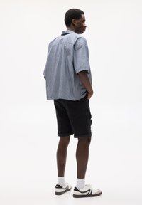 Chemise à manches courtes rayée en bleu et blanc, assortie à un short en denim noir. Les chaussures incluent des baskets blanches avec des accents noirs.
