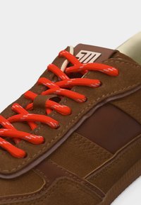 Καφέ σουέντ αθλητικό παπούτσι με πορτοκαλί κορδόνια, διακοσμημένο με λευκά διακεκομμένα σχέδια και ραμμένο δερμάτινο πάνελ.