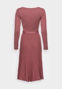 Robe en tricot rose poussière à manches longues avec corsage ajusté, jupe plissée et ceinture assortie, vue de dos sur fond blanc.