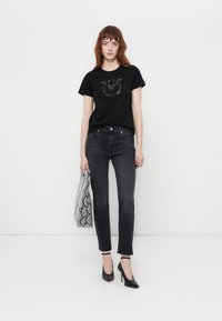 T-shirt noir avec un design graphique texturé, associé à un jean gris foncé et un sac à imprimé serpent. Des chaussures à talons hauts noires complètent le look.