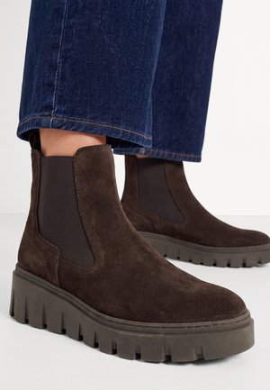 Bottines Chelsea en daim marron foncé avec semelles épaisses à crampons, portées avec un jean en denim bleu.