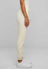 Joggers de color beige claro con cintura ajustable y puños en los tobillos, fabricados en un tejido suave. Combinados con zapatillas blancas para un look informal.