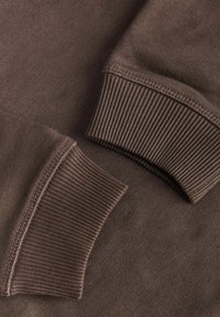Gros plan de deux manches de sweat marron montrant des poignets côtelés et des coutures détaillées sur un tissu doux.