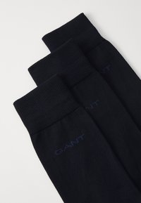 Mørkeblå sokker med ribbestrikkede mansjetter, laget av et mykt materiale. Har en subtil GANT-logo i blått. Tre par synlige, stablet.