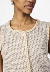 Beżowo-czarny top bez rękawów z tkaniny tweedowej, z plecionymi żółtymi wykończeniami, okrągłym dekoltem i złotymi guzikami z przodu.