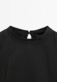 Tissu noir texturé avec un col rond et une petite fermeture par bouton au dos sur un vêtement.