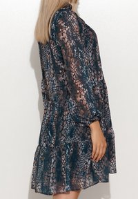 Abito a maniche lunghe in un tessuto trasparente e textured, caratterizzato da una stampa serpente blu e marrone, con orlo a strati con volant e vestibilità comoda.