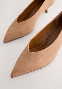 Escarpins en daim beige à bout pointu avec un petit talon. Dotés d'un design découpé sur la tige, dévoilant une doublure intérieure lisse.