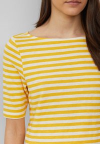 Haut à manches courtes rayé jaune et blanc avec un large décolleté et un tissu doux et texturé. Présente une coupe décontractée et un design minimaliste.