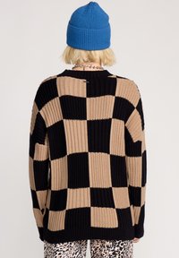 Stickad tröja med ett rutmönster i svart och beige, med ribbad textur och lös passform. Har rund halslinning och långa ärmar.
