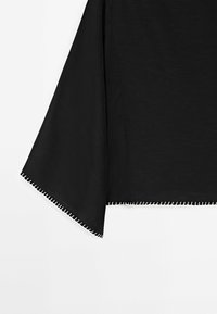 Vêtement noir avec des manches larges et tombantes. Texture lisse et design épuré, présentant un ourlet contrastant blanc cousu au bord.