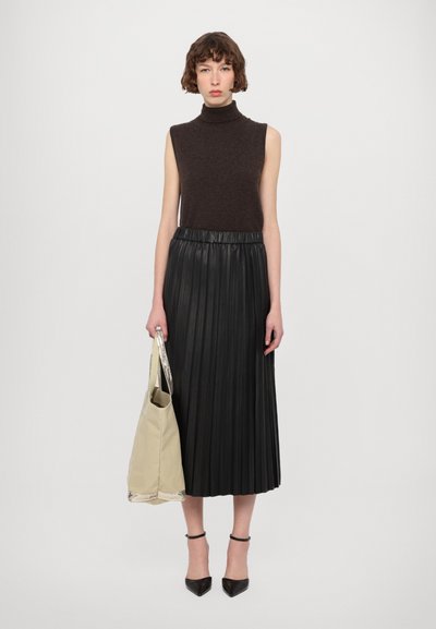 Top in maglia marrone senza maniche con collo alto abbinato a una gonna midi plissettata in finta pelle nera. Tiene una borsa tote beige con accenti argentati.