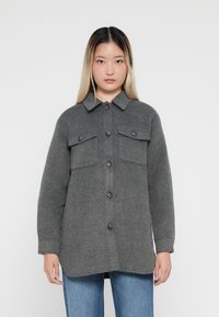 Grå ullblandad knäppjacka med två bröstfickor, en spetsig krage och en något rundad fåll. Bärs över denimjeans.