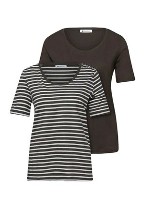 Two women wearing casual blue jeans and t-shirts stand side by side against a white wall; one holds a blue jacket.