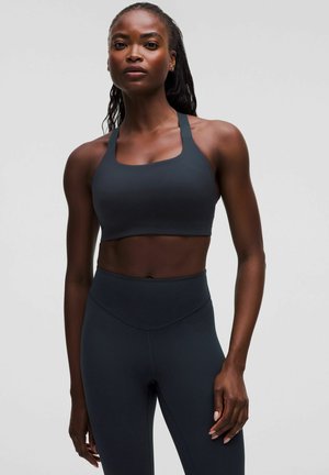 Sötét szürke sportmelltartó négyzetesnyakkivágással és vastag pántokkal, magas derekú sötét szürke leggings-szel párosítva, sima textúrával, testhezálló kialakítással.