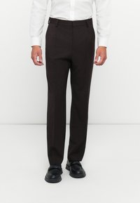 Pantaloni tăiați din material tartan maro, cu croi drept, având bucle pentru curea și buzunare, asortați cu pantofi negri slip-on.