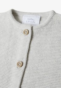 Cardigan lavorato a maglia grigio chiaro con una texture morbida, scollatura arrotondata e due bottoni di legno sul davanti. L'etichetta riporta "Stellou & friends."