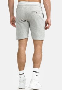 Grå shorts lavet af blødt stof, med en elastisk talje der kan justeres med snor, baglomme med knap og en afslappet pasform. Accentueret med hvide sokker og sneakers.