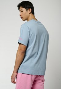 Lichtblauw katoenen T-shirt met korte mouwen, met een roze logodetail op de linkermouw. Soepele textuur, relaxte pasvorm.