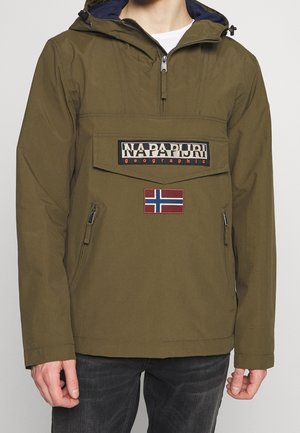 Mężczyzna noszący oliwkowo-zieloną kurtkę z kapturem zapinaną na zamek błyskawiczny z przodu, dużą kieszeń z patką oznaczoną napisem "Napapijri geographic" oraz naszywką z flagą Norwegii poniżej.