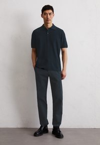 Granatowa koszulka polo z krótkim rękawem i kołnierzykiem, w połączeniu z ciemnoszarymi spodniami i czarnymi butami na sznurowadłach, na neutralnym tle.