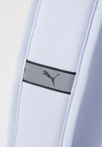 Lichtgrijze stof met een gestructureerd oppervlak, voorzien van een zwarte streep en een klein zwart Puma-logo in een springende positie.