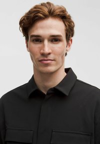 Mustanvärne särk kraega, millel on kaks esist pocketit. Kangas näib sile, kerge tekstuuri ja struktureeritud disainiga.