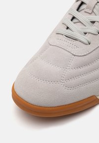 Lys grå semsket sneakers med en teksturert overdel, tonale sømmer og såle av gummi. Kjent for flate lisser og et rundet tådesign.