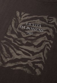 Napis "LA VITA DA BOHÈME Italy" nadrukowany na wyblakłym wzorze tygrysich pasków na ciemnej tkaninie.