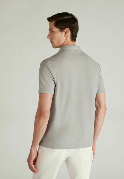 Polo grigio con maniche corte, texture liscia e colletto classico. Indossato da un modello maschile di spalle, abbinato a pantaloni bianchi.