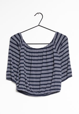 Blouse courte bleu marine avec des rayures horizontales blanches, encolure et ourlet élastiques, suspendue à un cintre noir en fil de fer.