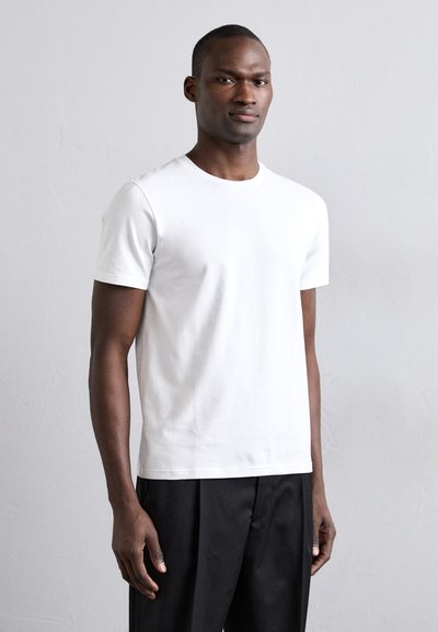 Weißes Baumwoll-T-Shirt mit Rundhalsausschnitt, kurzen Ärmeln, glatter Textur und schmaler Passform, kombiniert mit schwarzen Hosen.