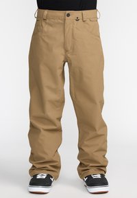 Pantalons cargo beiges avec une coupe décontractée, dotés d'une fermeture à bouton, de plusieurs poches et d'une texture lisse. Associés à des baskets noires.