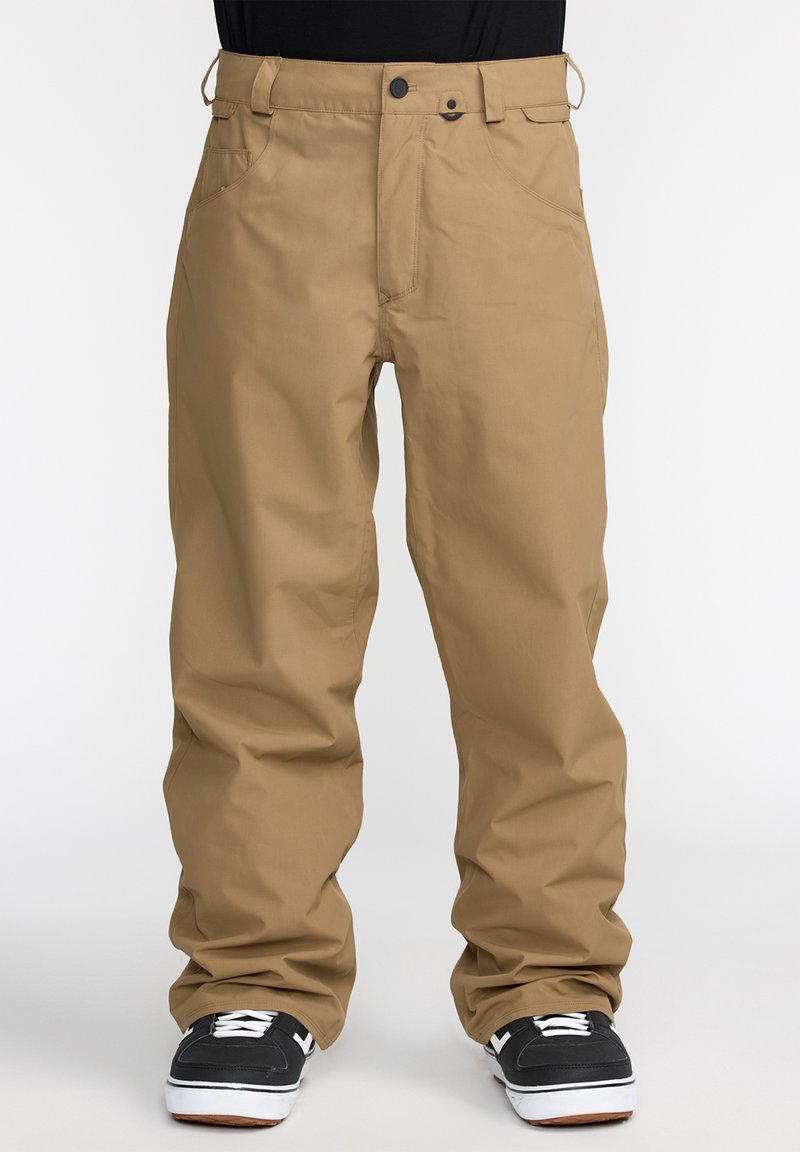 Pantalons cargo beiges avec une coupe décontractée, dotés d'une fermeture à bouton, de plusieurs poches et d'une texture lisse. Associés à des baskets noires.