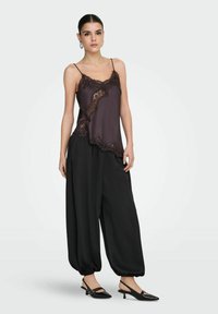 Tmavě fialové saténové tílko s krajkovým lemováním v kombinaci s černými plisovanými kalhotami a černými botami na podpatku se zadním páskem, s volným střihem a manžetami.