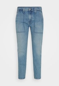 Světlé modré džíny s uvolněným střihem, které mají dvě přední kapsy, zapínání na knoflík a tapered nohavice.