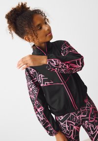Black jacket with pink scribble pattern, zip front, elastic cuffs, paired with matching leggings. Material appears smooth and lightweight.