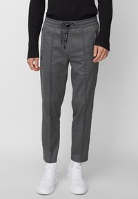 Grå byxor med en smal passform, elastisk midjeband med snörning, sidfickor och subtilt texturerad tyg; bärs med vita sneakers.