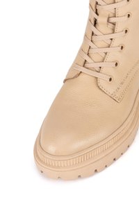 Beige kožené kotníkové boty s texturovaným povrchem, kulatou špičkou, šněrovacím designem a silnou, drsnou podrážkou pro lepší přilnavost.