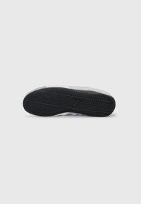 Semelle de sneaker avec un fond en caoutchouc noir texturé, tige en suède gris avec des accents blancs, conçue pour l'adhérence et la durabilité.
