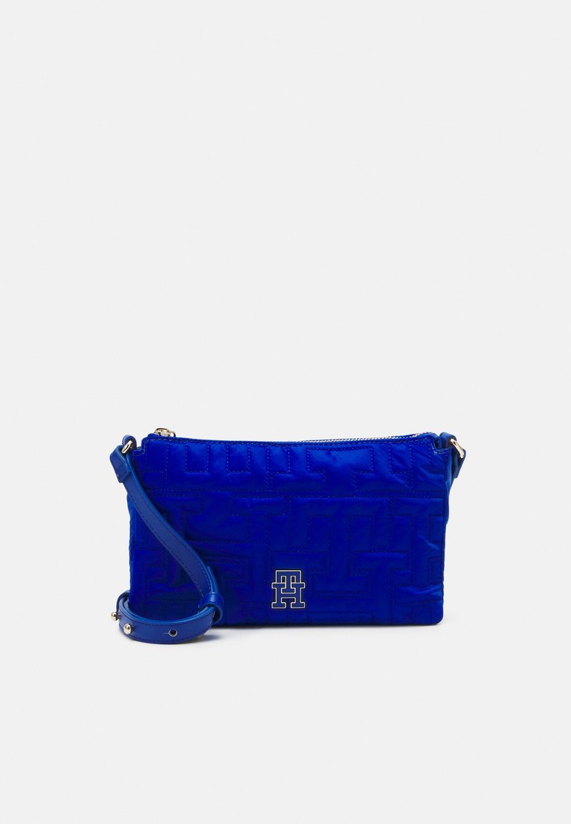 Kongelig blå quiltet crossbody taske med lynlås lukning, prydet med et logo og en aftagelig rem. Glat tekstur med en struktureret form.