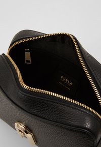 Borsa Furla in pelle nera a granello con apertura superiore a cerniera, che mostra l'interno foderato in tessuto e la chiusura lampo e il gancio in tonalità oro.