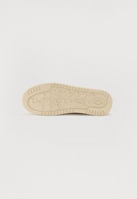 Semelle de chaussure en caoutchouc beige avec un motif de semelle et le texte "TOM TAILOR" embossé au centre, présentant des rainures horizontales et diagonales.
