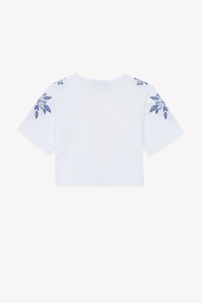 Λευκό cropped t-shirt με κοντά μανίκια, διακοσμημένο με μπλε κεντήματα με λουλούδια στους ώμους και στρογγυλή λαιμόκοψη.