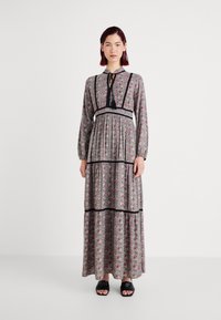 Robe maxi à imprimé floral avec manches longues, accents noirs et design en étages. Fabriquée en tissu léger, avec un détail de décolleté à nouer.