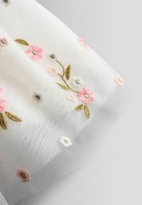 Weißer Tüllstoff mit zarten pinken und weißen Stickblumen sowie grünen Blättern, der eine weiche, durchsichtige Textur und filigrane Details aufweist.