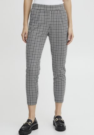 Pantalons gris à carreaux avec une coupe ajustée, taille élastique et légères plis. Portés avec des mocassins noirs accentués d'une boucle dorée.