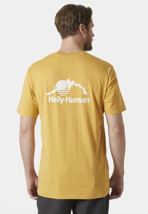Camiseta de algodón amarilla con un estampado en la espalda de montañas y un sol, con el logo de "Helly-Hansen" en blanco, mangas cortas y un corte relajado.
