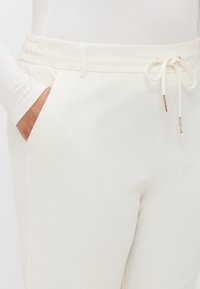 Hvide sweatpants med elastisk talje med snøre, sidelommer og en glat stoftekstur.