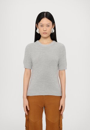 Maglione grigio a maniche corte con un motivo di lavorazione a maglia testurizzata. Collo e orlo a costine. Abbinato a pantaloni marroni con frange, creando un look a strati.